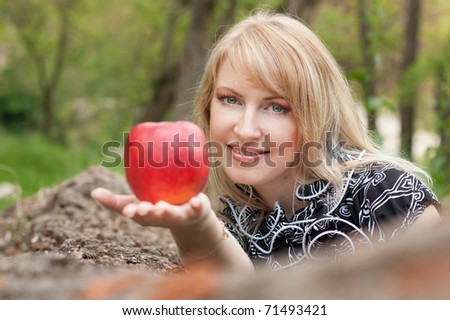 Beautiful smiling young woman with red apple in her hand outdoors, spring day