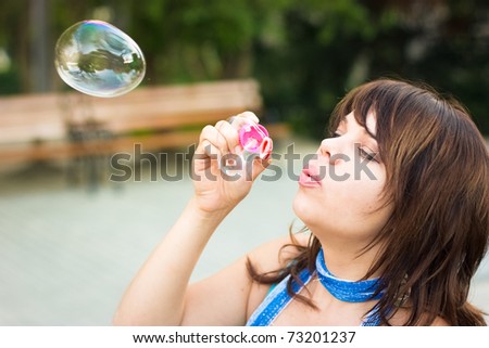 Beautiful young woman inflating soap bubbles outdoors