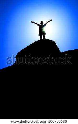 Silhouette of hiker at the top of a peak with blue sky in background
