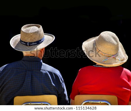 Old couple sitting in chairs wearing straw hats with black background
