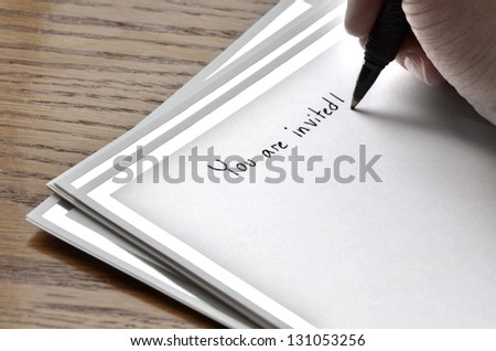 Person writing invitation on card with pen and ink
