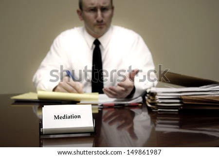Attorney at Law sitting at desk holding pen with files with a card for Mediation