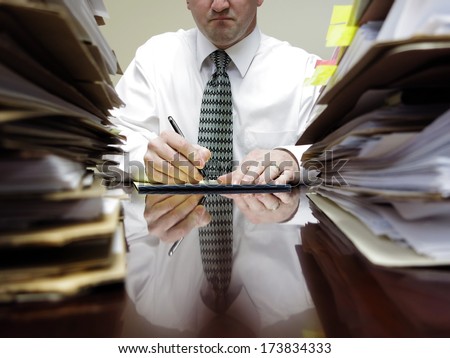 Businessman sitting at desk with pad of paper and piles files