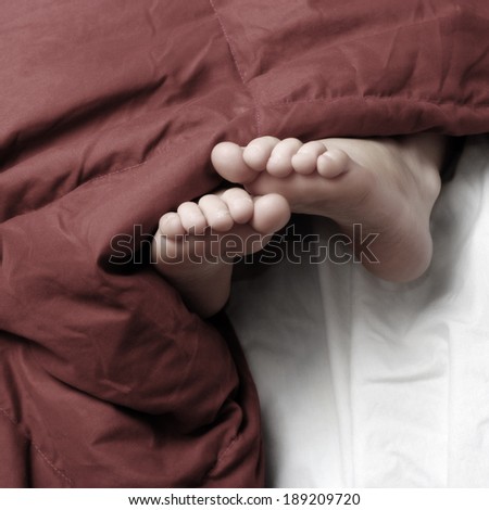 Person sleeping with feet poking out of red blankets on bed
