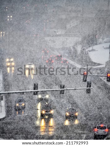 Snowy winter road with several cars driving on roadway with traffic lights