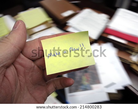 Messy office with hand holding note saying Make a Plan