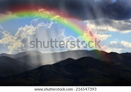 Sunlight rays from clouds falling on dark mountain range with Rainbow
