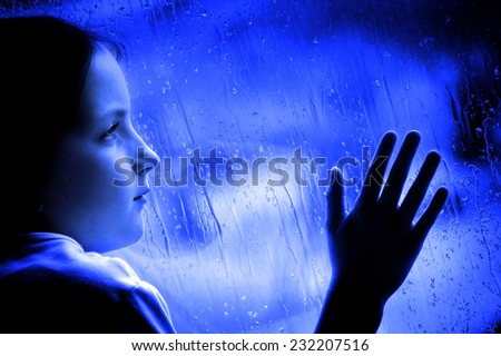 Girl looking out window on rainy day sad depressed feeling lonely