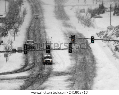 Snowy winter road with cars driving on roadway in snow storm and traffic lights