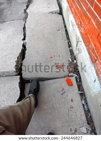 Man walking on broken dangerous cracked sidewalk and brick wall