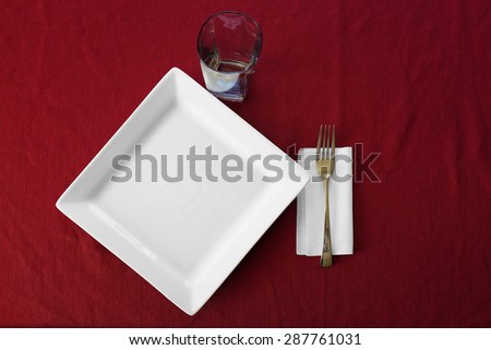 Detail of table place setting with plate cup fork and red table cloth