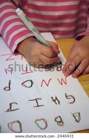 Little child writing on paper practicing writing letters of alphabet