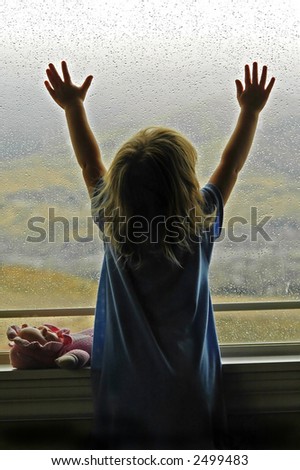 Little girl standing by window with raindrops on it on a rainy day