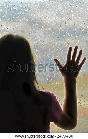 Little girl standing by window with raindrops on it on a rainy day