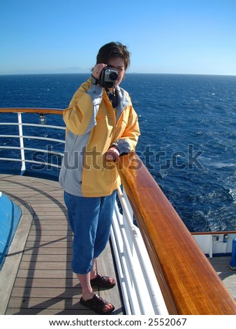Tourist woman on cruise ship wearing yellow jacket and holding video camera