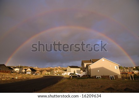 Colorful bright rainbow set against stormy sky over houses
