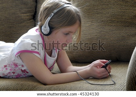 Little girl on couch listening to mp3 music with earphones