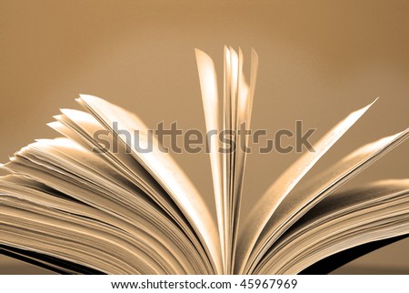A large single book sitting with pages open on a desk and brown background