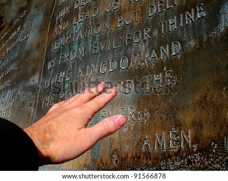 Hand reaching out to sculpture of the Lord\'s Prayer