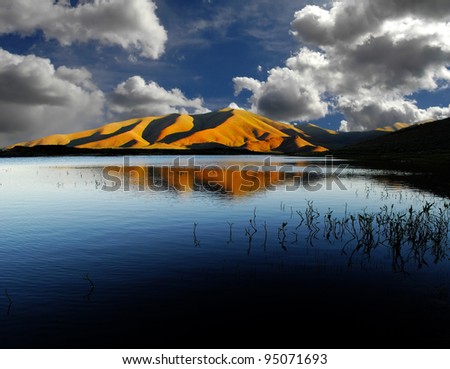 View of white and gray storm clouds in blue sky with rays of light above lake and mountains