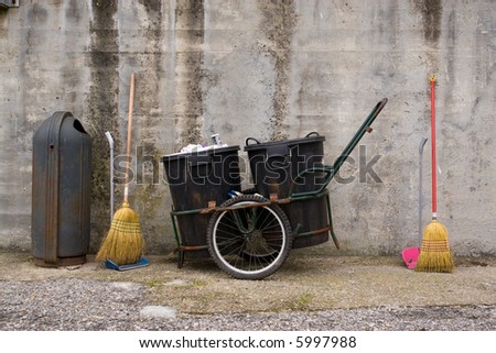 Car, brooms and shovels of a street cleaner next to an urban wastebasket