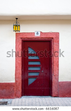 red door and yellow light in the facade of a house with number eight