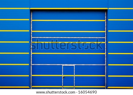 entrance of  blue industrial ship with horizontal  lines in yellow. A great inner door for the entrance of great vehicles lodges a smaller pedestrian door. The set offers a modern and geometric aspect