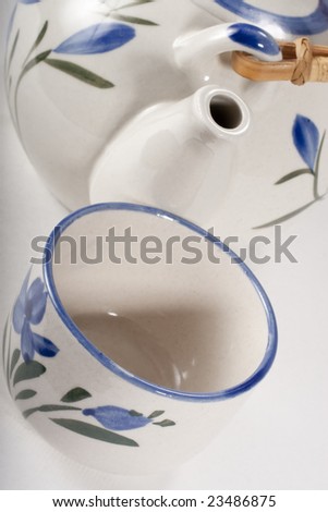 Tea-pot and cup of white porcelain refined decorated with floral motives in blue and green on white background
