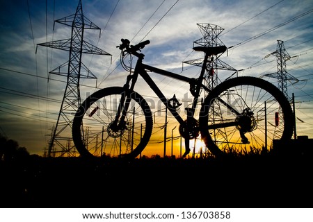 Bike Silhouette and high voltage power line towers on a field with beautiful sunset
