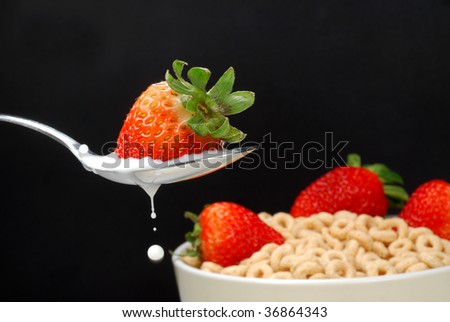 A Spoon with milk and a strawberry with a bowl of cereal and more strawberries behind