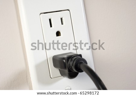 Image of black cable plugged in a white electric outlet mounted on a wall