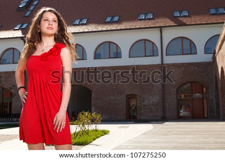 handsome girl dressed in red short skirt standing outside in urban landscape in a sunny day