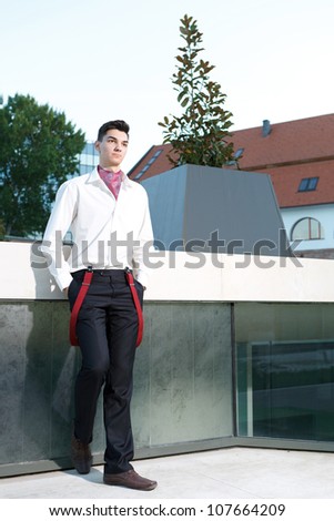 Handsome young hipster fashion male model wearing shirt and red braces posing outdoors