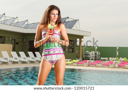 beautiful young sexy girl standing on pool side holding fresh cocktail drink with legs slightly apart