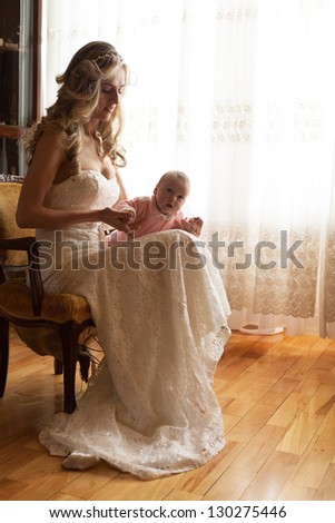 Happy mother playing with her baby daughter wearing wedding dress