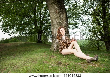 tired sexy girl with long legs resting against a tree wearing animal print clothes and heels