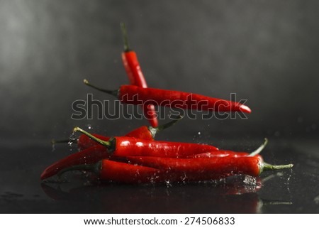 Red chilly peppers falling on wet stone surface and splashing