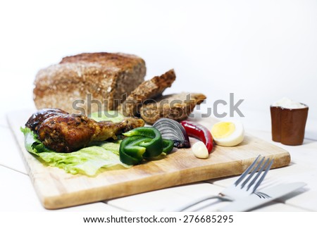 Oven baked drumstick on wood cutting board with vegetables and whole grain bread