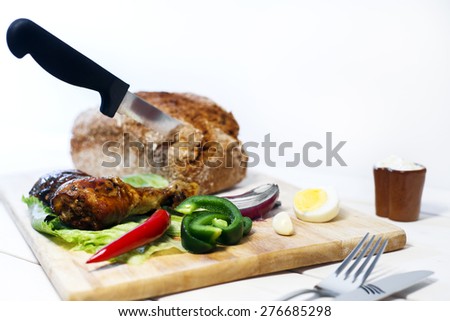 Oven baked drumstick on wood cutting board with vegetables and whole grain bread with knife in