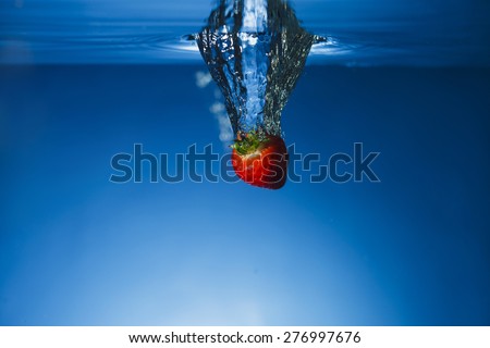 Single fresh Strawberry dropped in water tank and breaking the surface