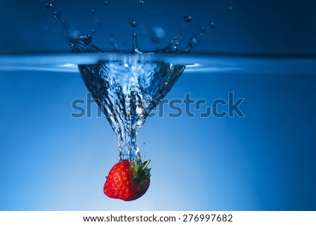 Single fresh Strawberry dropped in water tank and breaking the surface