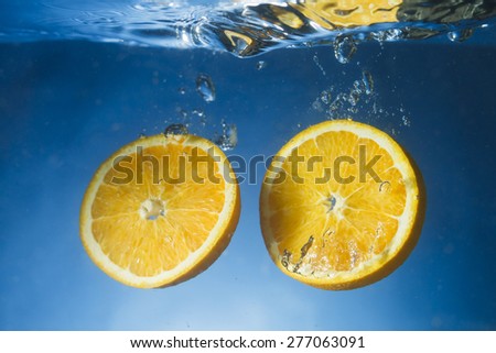 Orange slices dropped in crystal clear water with blue gradient background