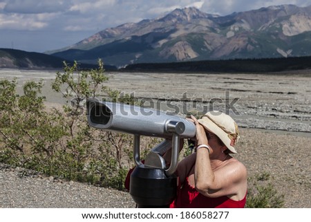 Female tourist looking through telescope for Dall sheep on hills in Denali National Park