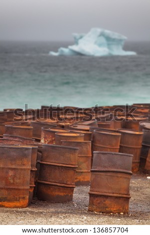 Rusty fuel and chemical drums on Arctic coast with iceberg on background