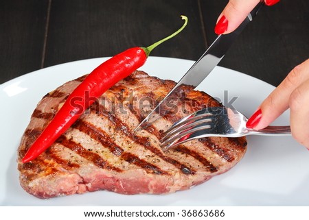 Juicy beef steak, fork and knife with woman\'s fingers with red manicure
