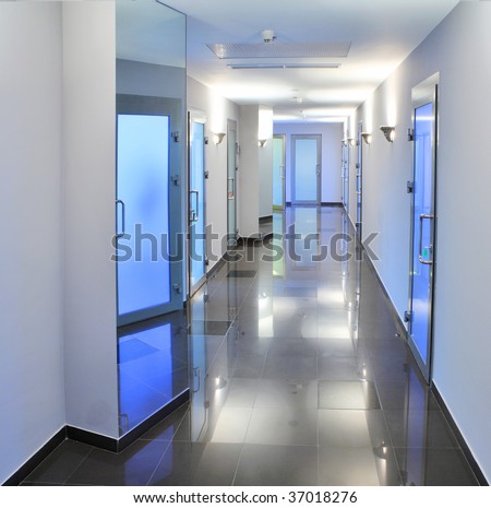 Long, empty corridor in a hospital or office building, with the ceiling lights reflected on the shiny floor.