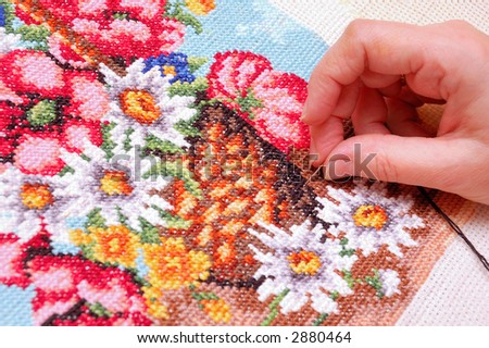 Woman embroidering a picture of flowers (cross stitch)