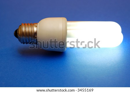 Energy efficient lit light bulb on blue background.