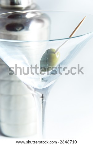 Olive sitting in Martini glass on white with cocktail shaker out of focus in background - short DOF. Cocktail shaker image in stem of glass