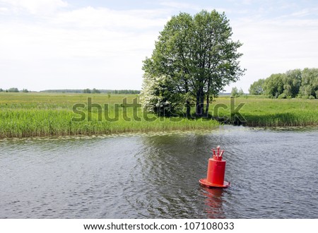 Red buoy beacon in lake shore water mark of ships swimming area. Meadow fields near lake.